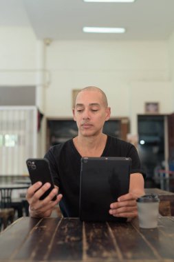 Siyah tişört giyen kel Latin bir adamın portresi, basit bir açık kahve dükkanında tek başına oturuyor.