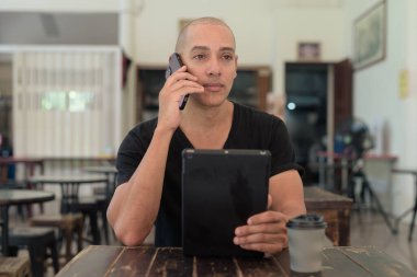 Siyah tişört giyen kel Latin bir adamın portresi, basit bir açık kahve dükkanında tek başına oturuyor.