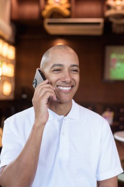 Beyaz polo tişörtlü kel Latin bir adamın portresi, şık bir Çin tarzı kahve dükkanında oturuyor, ev ortamında kendine güveni tam görünüyor..