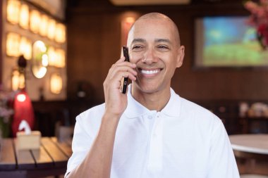 Beyaz polo tişörtlü kel Latin bir adamın portresi, şık bir Çin tarzı kahve dükkanında oturuyor, ev ortamında kendine güveni tam görünüyor..
