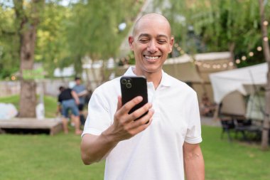 Beyaz polo tişörtlü şık kel bir adam kamp alanında karavanın yanında dinleniyor. Açık hava seyahati ve kamp yaşam tarzı konsepti çimenli çevre ve doğal ışık.