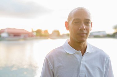 Kel yakışıklı İtalyan adamın yaz portresi. Gün batımında park gölünün yanında objektifle parlıyor.