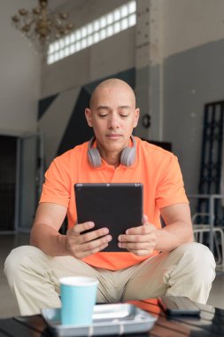 Kafe masasında kahve fincanı takan, kulaklık takan ve dijital tablet bilgisayar kullanan orta yaşlı yakışıklı bir adam. Teknoloji ve günlük yaşam tarzı kavramı.