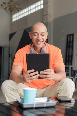 Kafe masasında kahve fincanı takan, kulaklık takan ve dijital tablet bilgisayar kullanan orta yaşlı yakışıklı bir adam. Teknoloji ve günlük yaşam tarzı kavramı.