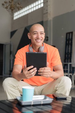 Kafe masasında kahve fincanı takan, kulaklık takan ve dijital tablet bilgisayar kullanan orta yaşlı yakışıklı bir adam. Teknoloji ve günlük yaşam tarzı kavramı.