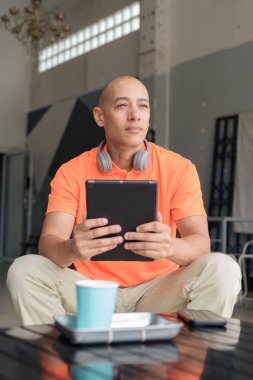 Kafe masasında kahve fincanı takan, kulaklık takan ve dijital tablet bilgisayar kullanan orta yaşlı yakışıklı bir adam. Teknoloji ve günlük yaşam tarzı kavramı.