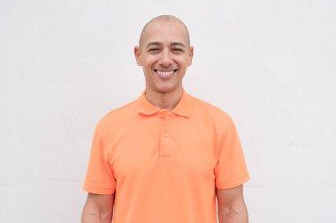 Orta yaşlı, turuncu polo tişörtlü, beyaz duvarlı yakışıklı bir İspanyol 'un stüdyo portresi. Günlük yaşam tarzı ve moda konsepti.