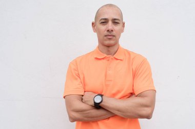 Orta yaşlı, turuncu polo tişörtlü, beyaz duvarlı yakışıklı bir İspanyol 'un stüdyo portresi. Günlük yaşam tarzı ve moda konsepti.