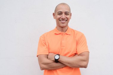 Orta yaşlı, turuncu polo tişörtlü, beyaz duvarlı yakışıklı bir İspanyol 'un stüdyo portresi. Günlük yaşam tarzı ve moda konsepti.