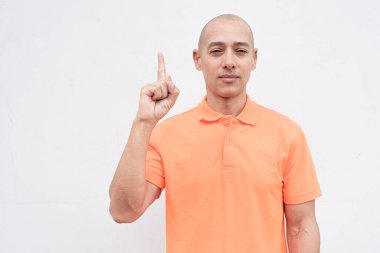 Orta yaşlı, turuncu polo tişörtlü, beyaz duvarlı yakışıklı bir İspanyol 'un stüdyo portresi. Günlük yaşam tarzı ve moda konsepti.