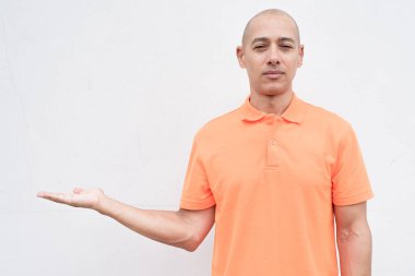 Orta yaşlı, turuncu polo tişörtlü, beyaz duvarlı yakışıklı bir İspanyol 'un stüdyo portresi. Günlük yaşam tarzı ve moda konsepti.