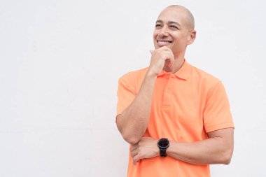 Orta yaşlı, turuncu polo tişörtlü, beyaz duvarlı yakışıklı bir İspanyol 'un stüdyo portresi. Günlük yaşam tarzı ve moda konsepti.