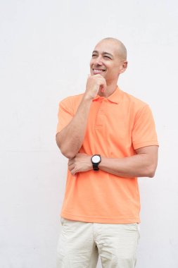 Orta yaşlı, turuncu polo tişörtlü, beyaz duvarlı yakışıklı bir İspanyol 'un stüdyo portresi. Günlük yaşam tarzı ve moda konsepti.