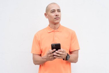 Orta yaşlı, turuncu polo tişörtlü, beyaz duvarlı yakışıklı bir İspanyol 'un stüdyo portresi. Günlük yaşam tarzı ve moda konsepti.