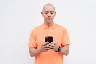 Orta yaşlı, turuncu polo tişörtlü, beyaz duvarlı yakışıklı bir İspanyol 'un stüdyo portresi. Günlük yaşam tarzı ve moda konsepti.