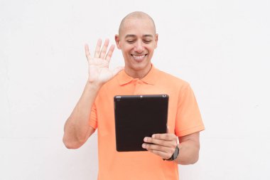 Portakal rengi polo tişörtlü yakışıklı, orta yaşlı, kel bir adamın dijital tablet bilgisayar kullanarak beyaz duvar arkaplanının stüdyo portresi. Günlük yaşam tarzı ve moda konsepti.