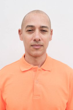Orta yaşlı, turuncu polo tişörtlü, beyaz duvarlı yakışıklı bir İspanyol 'un stüdyo portresi. Günlük yaşam tarzı ve moda konsepti.
