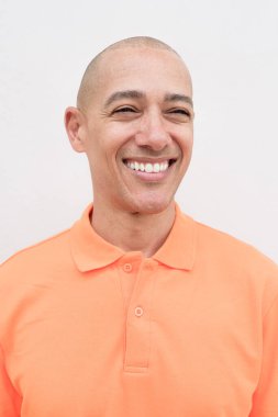 Orta yaşlı, turuncu polo tişörtlü, beyaz duvarlı yakışıklı bir İspanyol 'un stüdyo portresi. Günlük yaşam tarzı ve moda konsepti.