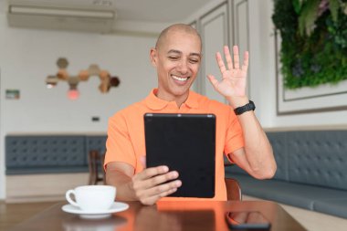 Kafe masasında kahve fincanı takan, kulaklık takan ve dijital tablet bilgisayar kullanan orta yaşlı yakışıklı bir adam. Teknoloji ve günlük yaşam tarzı kavramı.