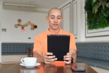 Kafe masasında kahve fincanı takan, kulaklık takan ve dijital tablet bilgisayar kullanan orta yaşlı yakışıklı bir adam. Teknoloji ve günlük yaşam tarzı kavramı.