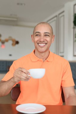 Orta yaşlı, turuncu polo tişörtlü, kahve fincanı tutan yakışıklı, kel bir İtalyan. Günlük yaşam tarzı kavramı.