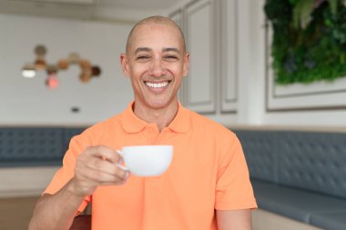 Orta yaşlı, turuncu polo tişörtlü, kahve fincanı tutan yakışıklı, kel bir İtalyan. Günlük yaşam tarzı kavramı.