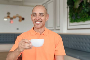 Orta yaşlı, turuncu polo tişörtlü, kahve fincanı tutan yakışıklı, kel bir İtalyan. Günlük yaşam tarzı kavramı.