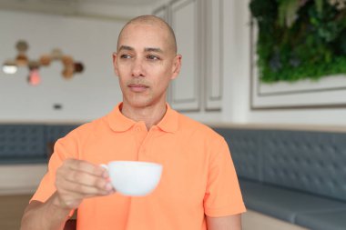 Kafe masasında kahve fincanı tutan orta yaşlı, turuncu polo tişörtlü yakışıklı, kel bir İtalyan. Günlük yaşam tarzı kavramı.