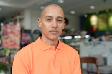 Kafe masasında oturan orta yaşlı, turuncu polo tişörtlü yakışıklı, kel bir İtalyan. Günlük yaşam tarzı kavramı.