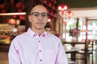 40 'lı yaşlarda kel, olgun bir erkek. Çin tarzı çay evinde pembe günlük iş gömleği ve gözlük takıyor. Kültür, rahatlama ve yaşam tarzı kavramı.