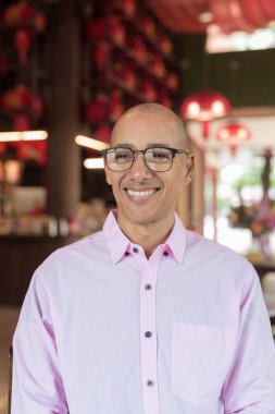 40 'lı yaşlarda kel, olgun bir erkek. Çin tarzı çay evinde pembe günlük iş gömleği ve gözlük takıyor. Kültür, rahatlama ve yaşam tarzı kavramı.