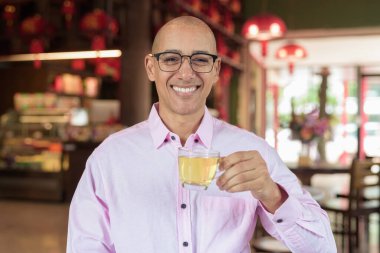 40 'lı yaşlarda kel, olgun bir erkek. Çin tarzı çay evinde pembe günlük iş gömleği ve gözlük takıyor. Kültür, rahatlama ve yaşam tarzı kavramı.