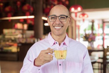 40 'lı yaşlarda kel, olgun bir erkek. Çin tarzı çay evinde pembe günlük iş gömleği ve gözlük takıyor. Kültür, rahatlama ve yaşam tarzı kavramı.