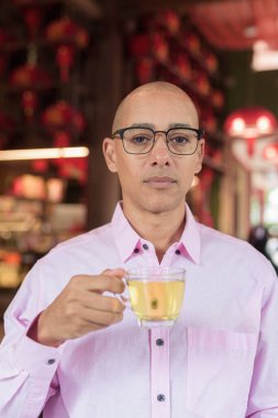 40 'lı yaşlarda kel, olgun bir erkek. Çin tarzı çay evinde pembe günlük iş gömleği ve gözlük takıyor. Kültür, rahatlama ve yaşam tarzı kavramı.