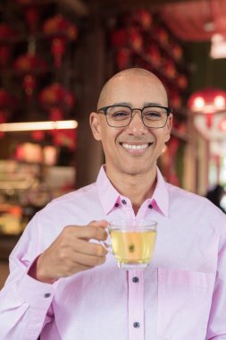 40 'lı yaşlarda kel, olgun bir erkek. Çin tarzı çay evinde pembe günlük iş gömleği ve gözlük takıyor. Kültür, rahatlama ve yaşam tarzı kavramı.