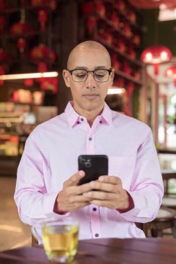 40 'lı yaşlarda kel, olgun bir erkek. Çin tarzı çay evinde pembe günlük iş gömleği ve gözlük takıyor. Kültür, rahatlama ve yaşam tarzı kavramı.