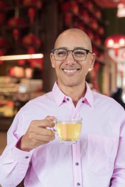 40 'lı yaşlarda kel, olgun bir erkek. Çin tarzı çay evinde pembe günlük iş gömleği ve gözlük takıyor. Kültür, rahatlama ve yaşam tarzı kavramı.