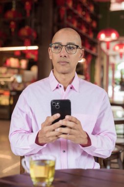 40 'lı yaşlarda kel, olgun bir erkek. Çin tarzı çay evinde pembe günlük iş gömleği ve gözlük takıyor. Kültür, rahatlama ve yaşam tarzı kavramı.