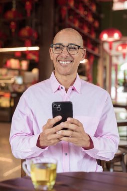 40 'lı yaşlarda kel, olgun bir erkek. Çin tarzı çay evinde pembe günlük iş gömleği ve gözlük takıyor. Kültür, rahatlama ve yaşam tarzı kavramı.