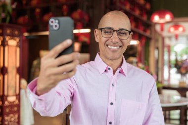 40 'lı yaşlarda kel, olgun bir erkek. Çin tarzı çay evinde pembe günlük iş gömleği ve gözlük takıyor. Kültür, rahatlama ve yaşam tarzı kavramı.