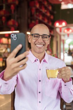 40 'lı yaşlarda kel, olgun bir erkek. Çin tarzı çay evinde pembe günlük iş gömleği ve gözlük takıyor. Kültür, rahatlama ve yaşam tarzı kavramı.