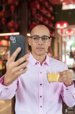 40 'lı yaşlarda kel, olgun bir erkek. Çin tarzı çay evinde pembe günlük iş gömleği ve gözlük takıyor. Kültür, rahatlama ve yaşam tarzı kavramı.