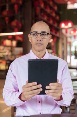 40 'lı yaşlarda kel, olgun bir erkek. Çin tarzı çay evinde pembe günlük iş gömleği ve gözlük takıyor. Kültür, rahatlama ve yaşam tarzı kavramı.