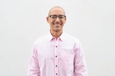 40 'lı yaşlarda, kel, olgun bir erkek. Sıradan pembe iş gömleği ve gözlük takıyor. Düz beyaz duvarın önünde duruyor. Şirket, iş ve yaşam tarzı kavramları için stüdyo tarzı görüntü kullanışlıdır.