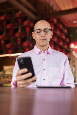 40 'lı yaşlarda kel, olgun bir erkek. Çin tarzı çay evinde pembe günlük iş gömleği ve gözlük takıyor. Kültür, rahatlama ve yaşam tarzı kavramı.