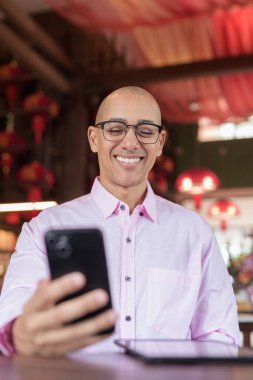 40 'lı yaşlarda kel, olgun bir erkek. Çin tarzı çay evinde pembe günlük iş gömleği ve gözlük takıyor. Kültür, rahatlama ve yaşam tarzı kavramı.