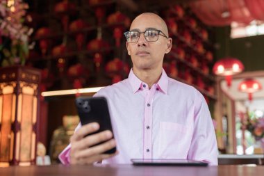 40 'lı yaşlarda kel, olgun bir erkek. Çin tarzı çay evinde pembe günlük iş gömleği ve gözlük takıyor. Kültür, rahatlama ve yaşam tarzı kavramı.