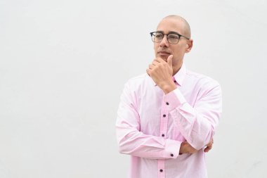 40 'lı yaşlarda, kel, olgun bir erkek. Sıradan pembe iş gömleği ve gözlük takıyor. Düz beyaz duvarın önünde duruyor. Şirket, iş ve yaşam tarzı kavramları için stüdyo tarzı görüntü kullanışlıdır.