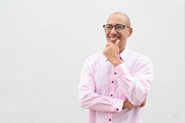 40 'lı yaşlarda, kel, olgun bir erkek. Sıradan pembe iş gömleği ve gözlük takıyor. Düz beyaz duvarın önünde duruyor. Şirket, iş ve yaşam tarzı kavramları için stüdyo tarzı görüntü kullanışlıdır.