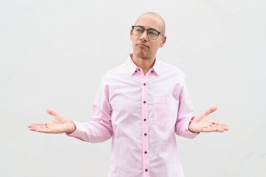 40 'lı yaşlarda, kel, olgun bir erkek. Sıradan pembe iş gömleği ve gözlük takıyor. Düz beyaz duvarın önünde duruyor. Şirket, iş ve yaşam tarzı kavramları için stüdyo tarzı görüntü kullanışlıdır.